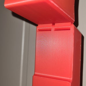 May include: A red 3D printed object with a hinged lid. The object is made up of two rectangular boxes stacked on top of each other.