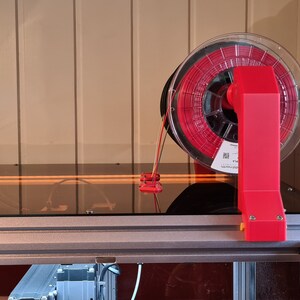 May include: A red filament spool holder attached to a 3D printer. The spool is clear and contains red filament.