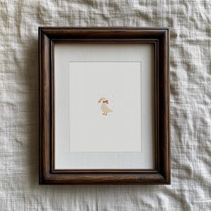 May include: A framed print featuring a whimsical illustration of a goose with a red bow and berries in its beak. The artwork is set against a white background, framed in a dark brown wooden frame. The overall aesthetic is charming and rustic.