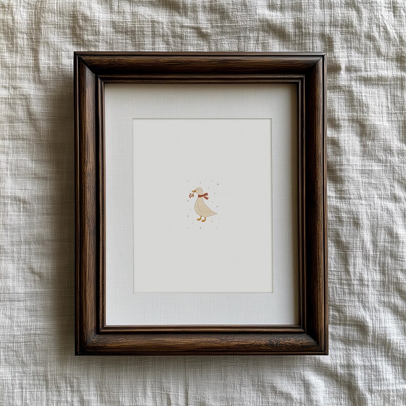 May include: A framed print featuring a whimsical illustration of a goose with a red bow and berries in its beak. The artwork is set against a white background, framed in a dark brown wooden frame. The overall aesthetic is charming and rustic.
