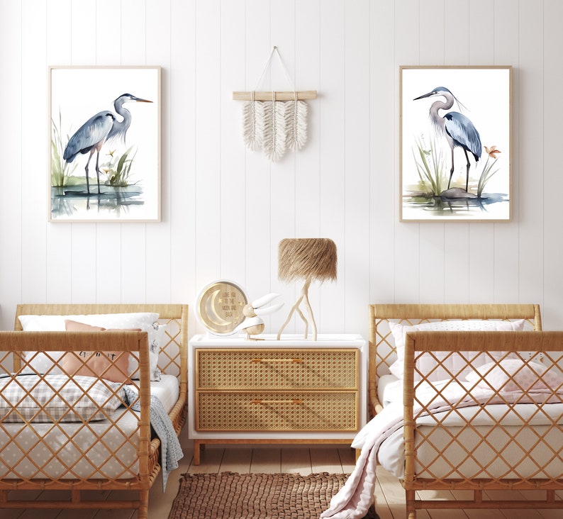 May include: Two watercolor paintings of blue herons standing in a marsh setting, framed in natural wood, hanging on a white wall above two wicker twin beds with white bedding and a woven rug on the floor.
