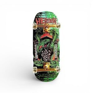 Peut inclure: Une planche à doigts verte et noire avec le mot "HEROIN" en rouge. La planche présente un graphisme de dragon et de piliers. Les roues et le matériel sont de couleur or.
