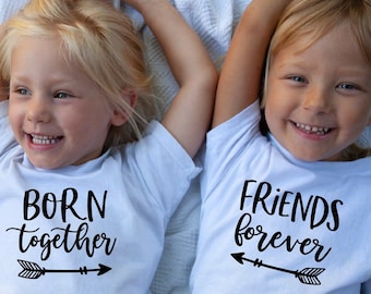 Może przedstawiać: Dwoje dzieci w białych koszulkach z czarnym tekstem i strzałkami. Dziecko po lewej stronie ma napis "BORN together", a dziecko po prawej stronie ma napis "FRIENDS forever".