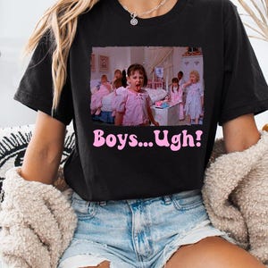 May include: Black t-shirt with a pink graphic that says "Boys...Ugh!" The graphic is a still from a movie scene. The shirt is worn with denim shorts and a cream-colored sweater.