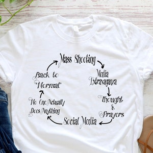 May include: White t-shirt with a black graphic design of a cycle of events related to mass shootings. The graphic includes the text "Mass Shooting", "Media Frenzy", "Back to Normal", "No One Actually Does Anything", "Social Media", "Thoughts & Prayers".