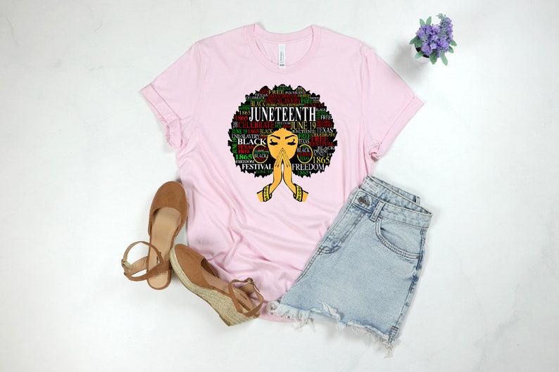 May include: Pink t-shirt with a black and green graphic of a woman's face with an afro hairstyle. The graphic is made up of words related to Juneteenth, including "Juneteenth", "Freedom", "Black", and "1865".