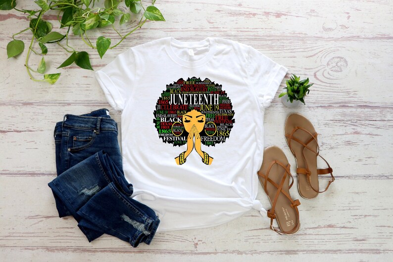 May include: White t-shirt with a black and green graphic of a woman's face with an afro hairstyle. The afro is made up of words related to Juneteenth, including "Juneteenth", "Celebrate", "Freedom", "1865", and "Black".