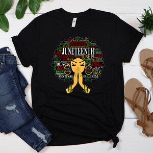May include: Black t-shirt with a graphic of a woman's afro hair styled with the words "Juneteenth" and other related words in red, green, and yellow.