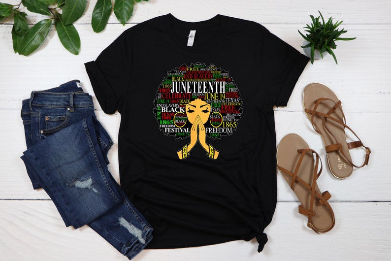 May include: Black t-shirt with a graphic of a woman's afro hair styled with the words "Juneteenth" and other related words in red, green, and yellow.
