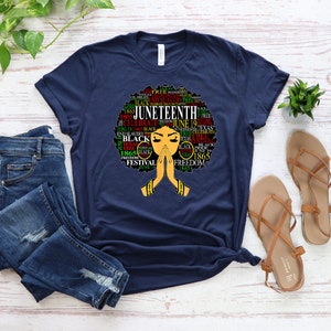 May include: A navy blue t-shirt with a graphic of a black woman's afro hair styled with the words "Juneteenth" and other related words in red, green, and yellow.