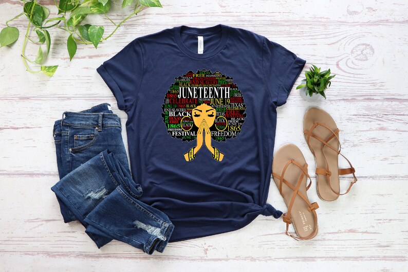 May include: A navy blue t-shirt with a graphic of a black woman's afro hair styled with the words "Juneteenth" and other related words in red, green, and yellow.