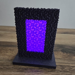 Op de afbeelding: Een 3D-geprint model van een Minecraft Nether-portaal met een gloeiend paars licht dat uit het portaal straalt.
