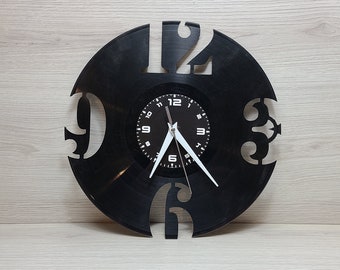 May include: A black vinyl record clock with white numbers and hands. The clock face is a smaller circle in the center of the record with black numbers and hands.