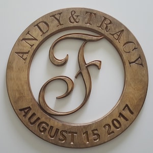 Peut inclure: Une plaque ronde en bois avec le texte "Andy & Tracy August 15 2017" autour du bord. Une grande lettre "F" stylisée est au centre de la plaque.