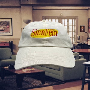 May include: A white baseball cap with a yellow oval and the text "Sinn Féin" in red lettering.