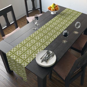 May include: A green and white geometric patterned table runner on a dark wood table with two chairs and a bowl of fruit.