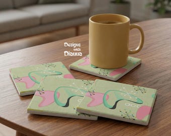 May include: A set of four square coasters with a retro design featuring pink, teal, and black shapes on a light green background. A yellow mug sits on one coaster. The text "Designs with Dianna" is visible.