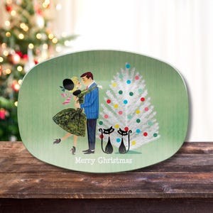 May include: A green oval serving platter with a vintage illustration of a couple kissing in front of a white Christmas tree with colorful ornaments. Two black cats are sitting in front of the tree. The text "Merry Christmas" is printed on the platter.