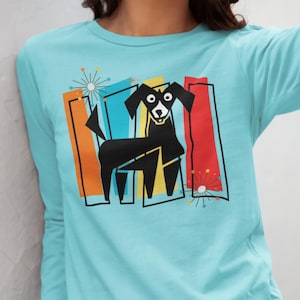 Puede incluir: Una camiseta de manga larga de color azul claro con un estampado gráfico de un perro negro con marcas blancas en la cara. El diseño incluye barras rectangulares verticales naranjas, azules, amarillas y rojas, con dos estrellas de puntos.