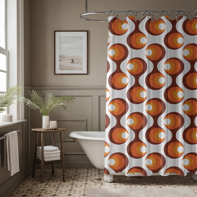 May include: A retro-style shower curtain with a repeating pattern of brown, orange, and white circular shapes. The curtain hangs in a bathroom with a white bathtub, a small wooden table, and a framed picture on the wall.