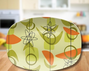 May include: An oval serving platter featuring a light green background with a repeating pattern of black atomic starburst symbols, solid orange semi-circles, and muted olive green abstract shapes, all connected by thin vertical black lines.