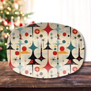 May include: An oval serving platter with a mid-century modern design. The cream-colored surface features a repeating pattern of stylized Christmas trees, starbursts, and geometric shapes in red, black, teal, yellow, and gray.