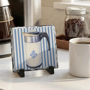 May include: A white ceramic mug with a black handle and the text "But First, Coffee" in a black, bold font. The mug is on a white surface.