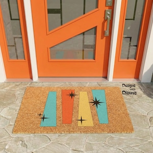 May include: A rectangular tan coir doormat featuring a mid-century modern pattern of four vertical trapezoidal shapes in teal, orange, and yellow. The design includes black starburst accents. The text Designs with Dianna is printed in black.