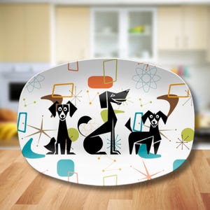 May include: An oval white serving platter featuring a graphic pattern of three black stylized dogs. The design includes colorful geometric shapes, including orange rectangles, teal boomerangs, green circles, and thin starburst line motifs.