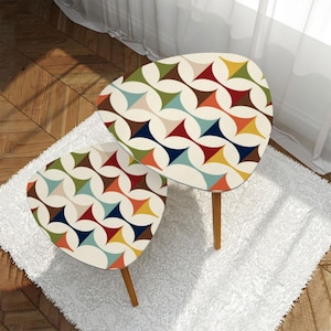 May include: Two mid-century modern accent tables with a cream-colored surface and a colorful geometric pattern. The tables have wooden legs and are placed on a white rug. The pattern includes shapes in blue, red, yellow, green, and brown.