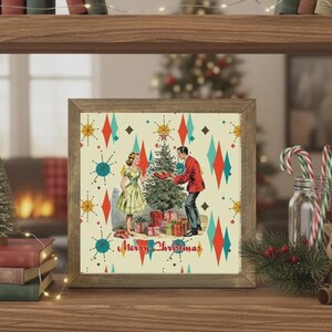 May include: A square framed print featuring a mid-century style illustration of two people decorating a Christmas tree with gifts underneath. The background has a cream color with red and teal starburst patterns and the text Merry Christmas.