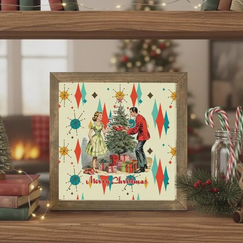 May include: A square framed print featuring a mid-century style illustration of two people decorating a Christmas tree with gifts underneath. The background has a cream color with red and teal starburst patterns and the text Merry Christmas.