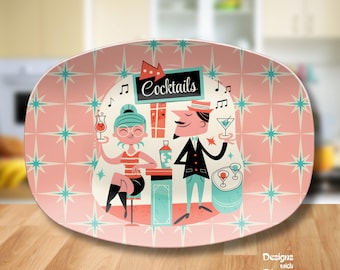 May include: Oval serving platter with a retro cocktail party design. The pink platter features a repeating starburst pattern and a central illustration of a man and woman at a bar with the word "Cocktails".