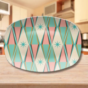 May include: A white oval serving dish with a retro geometric pattern in shades of pink, teal, brown, and gold. The pattern features repeating diamond shapes with a starburst design in the center of each diamond.