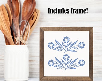 Puede incluir: Una impresión enmarcada con un diseño floral azul sobre un fondo blanco. El marco es de madera marrón. El texto "Includes frame!" es visible sobre la impresión.