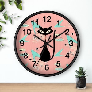 May include: A pink and black clock with a retro design featuring a black cat with a white collar and a turquoise blue background. The clock face has black numbers and hands.