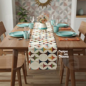 May include: A wooden dining table set for a meal, featuring a patterned table runner with geometric shapes in various colors. The table is set with teal plates, mugs, and glassware. The text "Designs with Dianna" is visible.