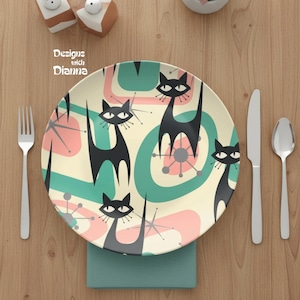 May include: A decorative plate with a retro cat design. The plate features black cat silhouettes, pink and teal abstract shapes, and starburst accents on a cream background. The text "Designs with Dianna" is visible.