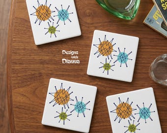 May include: Four square white coasters featuring a repeating graphic pattern of orange, light blue, and lime green starburst shapes connected by dark blue lines. The text Designs with Dianna is printed in white on the wooden surface.