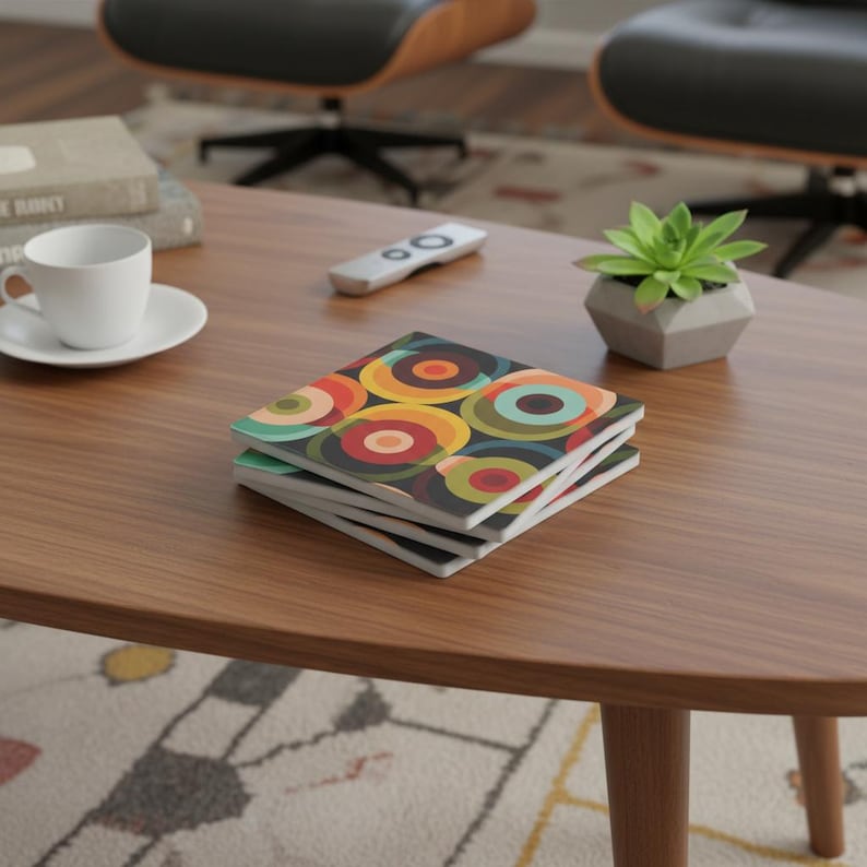May include: A stack of four square coasters with a retro, colorful circular pattern in shades of orange, yellow, red, teal, and green on a dark background. The coasters are on a wooden coffee table.