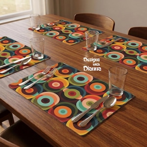 May include: Four rectangular placemats with a repeating pattern of concentric circles in shades of orange, teal, olive green, and dark brown. Each placemat features a clear glass, a silver fork, a silver knife, and a silver spoon. Text reads Designs with Dianna.