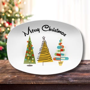 May include: White oval serving platter with the text "Merry Christmas" in black lettering. Three stylized Christmas trees are depicted in green, yellow, and blue with red and white accents.