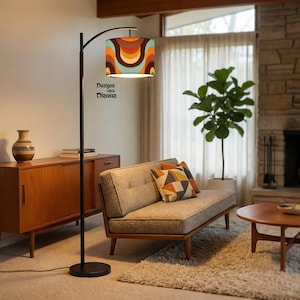 May include: A black arc floor lamp with a retro-style lampshade featuring a colorful pattern of orange, brown, and teal. The lamp is in a living room setting with a mid-century modern aesthetic. Text on the lampshade reads "Design with Dianna."