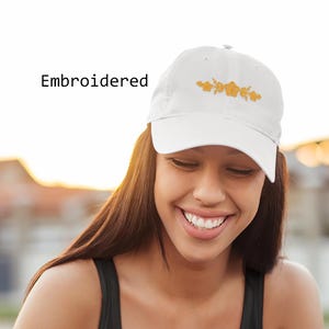 May include: White embroidered baseball cap with a gold floral design. The cap has a curved brim and an adjustable strap.