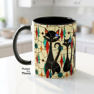 May include: A ceramic mug with a black handle and interior. The exterior features a stained-glass design with black cat figures and colorful geometric shapes. The mug has the text "Designs with Dianna" on the side.