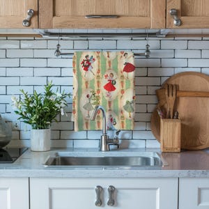 May include: A kitchen towel with a vintage design featuring illustrations of women in dresses. The towel has a green and cream striped background with oval frames. The women are wearing red, green, and cream dresses.