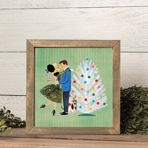 May include: A framed square print featuring a retro-style illustration of a couple dancing near a white Christmas tree decorated with colorful ornaments. A small dog sits at the base of the tree. The background is a textured light green.