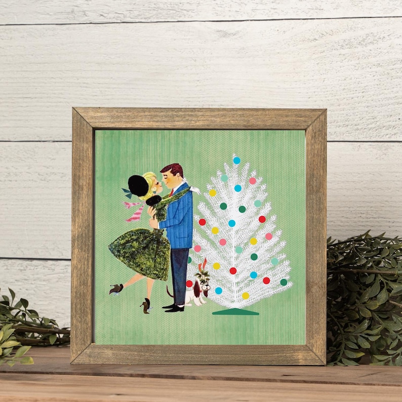 May include: A framed square print featuring a retro-style illustration of a couple dancing near a white Christmas tree decorated with colorful ornaments. A small dog sits at the base of the tree. The background is a textured light green.