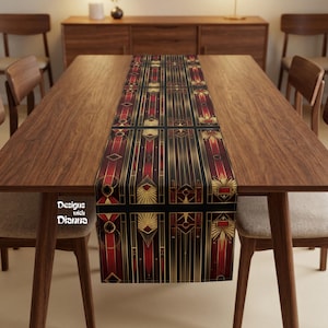 May include: A rectangular table runner with an Art Deco design. The runner features a black background with vertical gold lines and geometric shapes in red and gold. The runner is placed on a wooden table.
