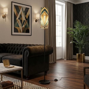 May include: A tall floor lamp with a slender black metal pole and a cylindrical shade featuring a geometric pattern in shades of dark green, cream, and gold. The lamp stands on a circular black base and includes a black power cord with a floor switch.